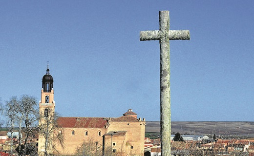 Cruz de piedra y, al fondo, la iglesia de Santa María. Villaverde de Medina